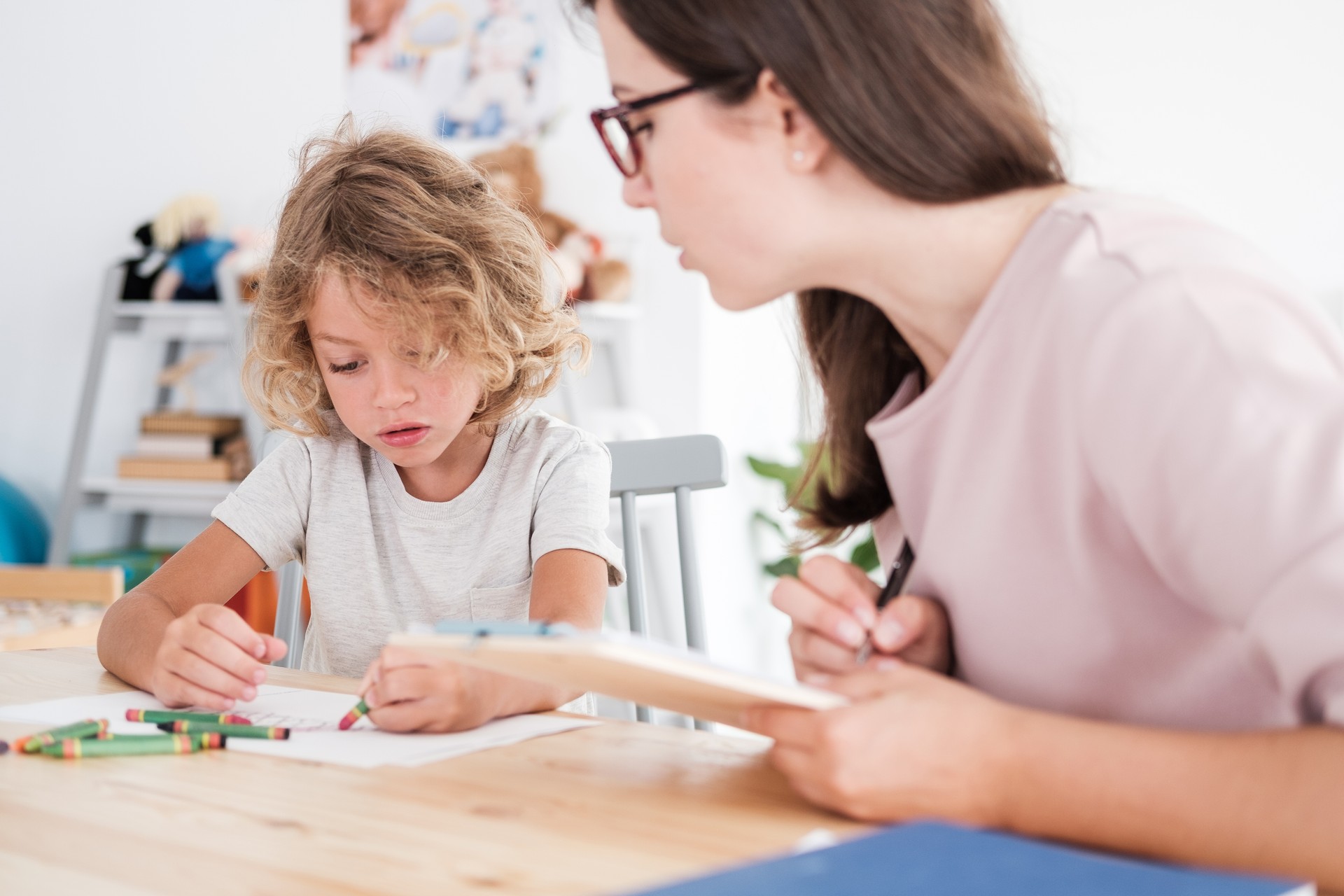 A psychotherapist watching a child draw pictures with crayons during an evaluation in a private school.