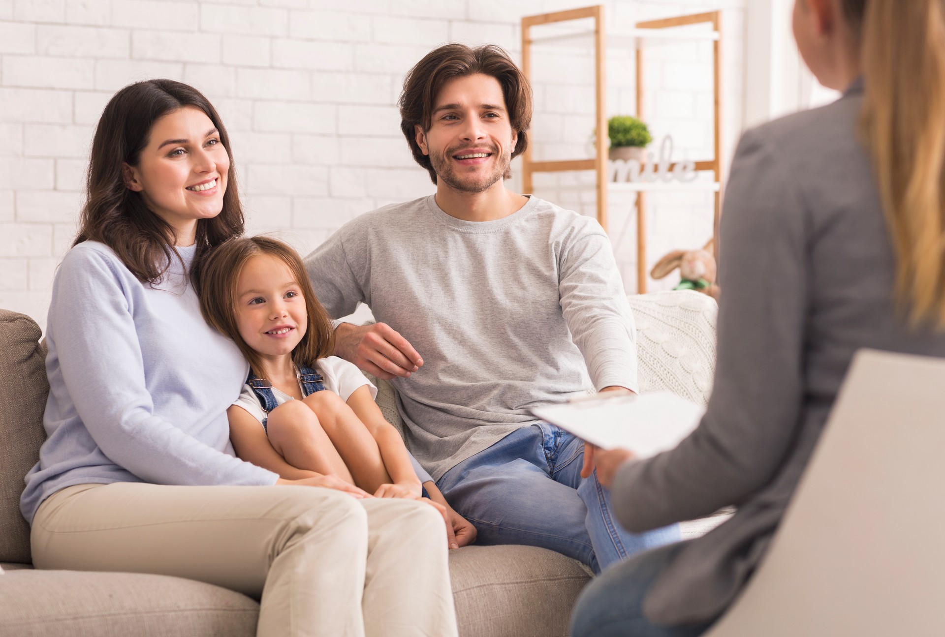 Parents With Little Daughter Sitting At Psycholigist's Office After Successful Therapy